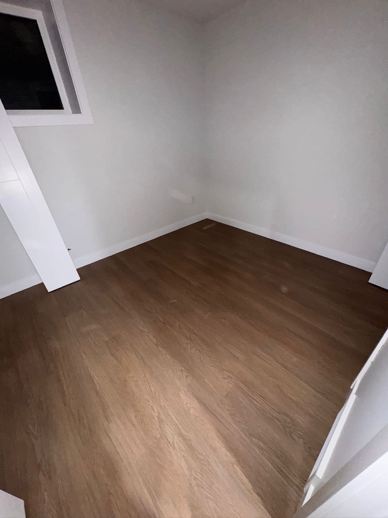 The same basement bedroom at handover, with vinyl plank flooring, cleaned walls, window and baseboards.