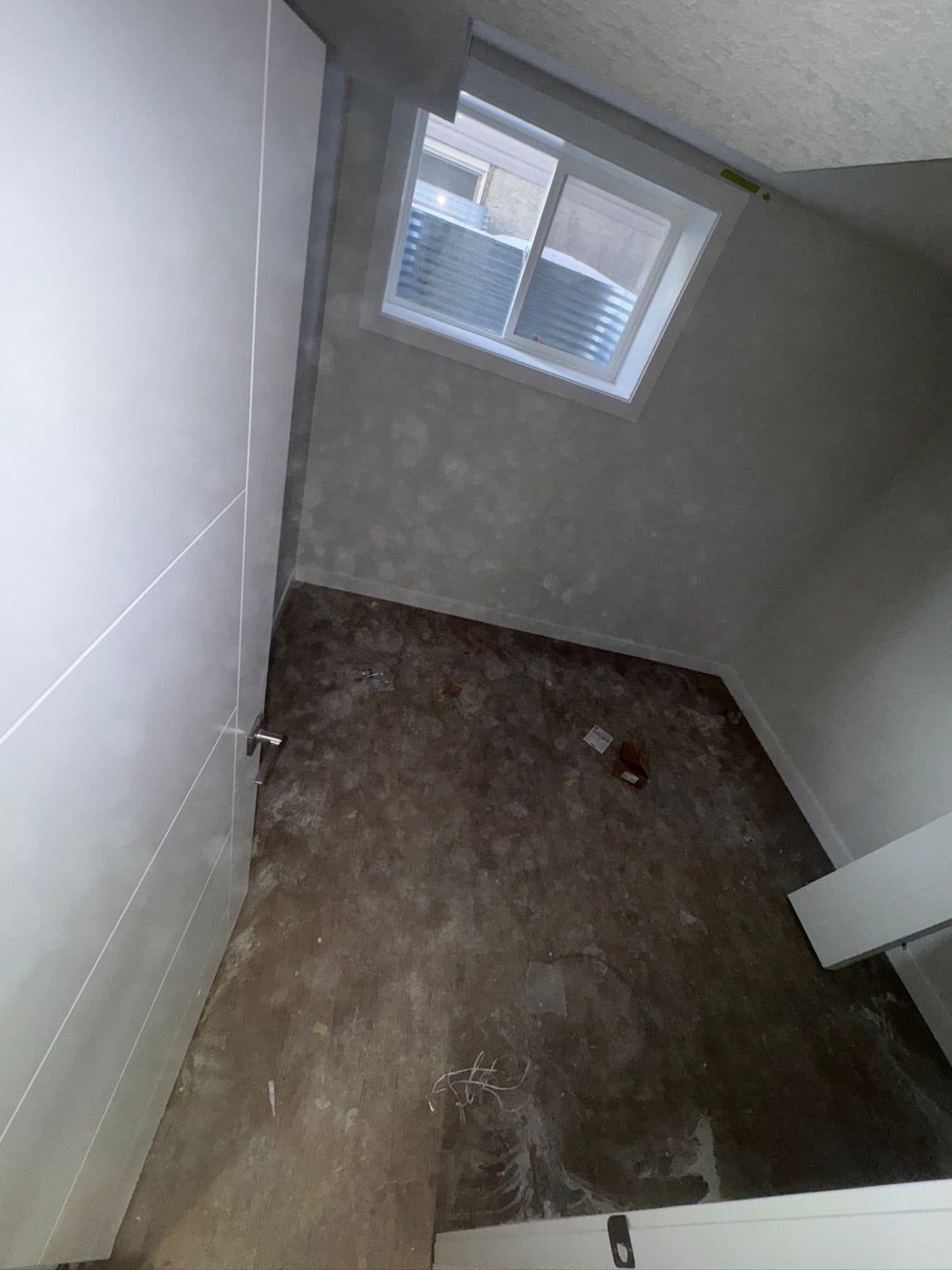 Basement bedroom at site condition: bare concrete subfloor, dust across the walls and window.