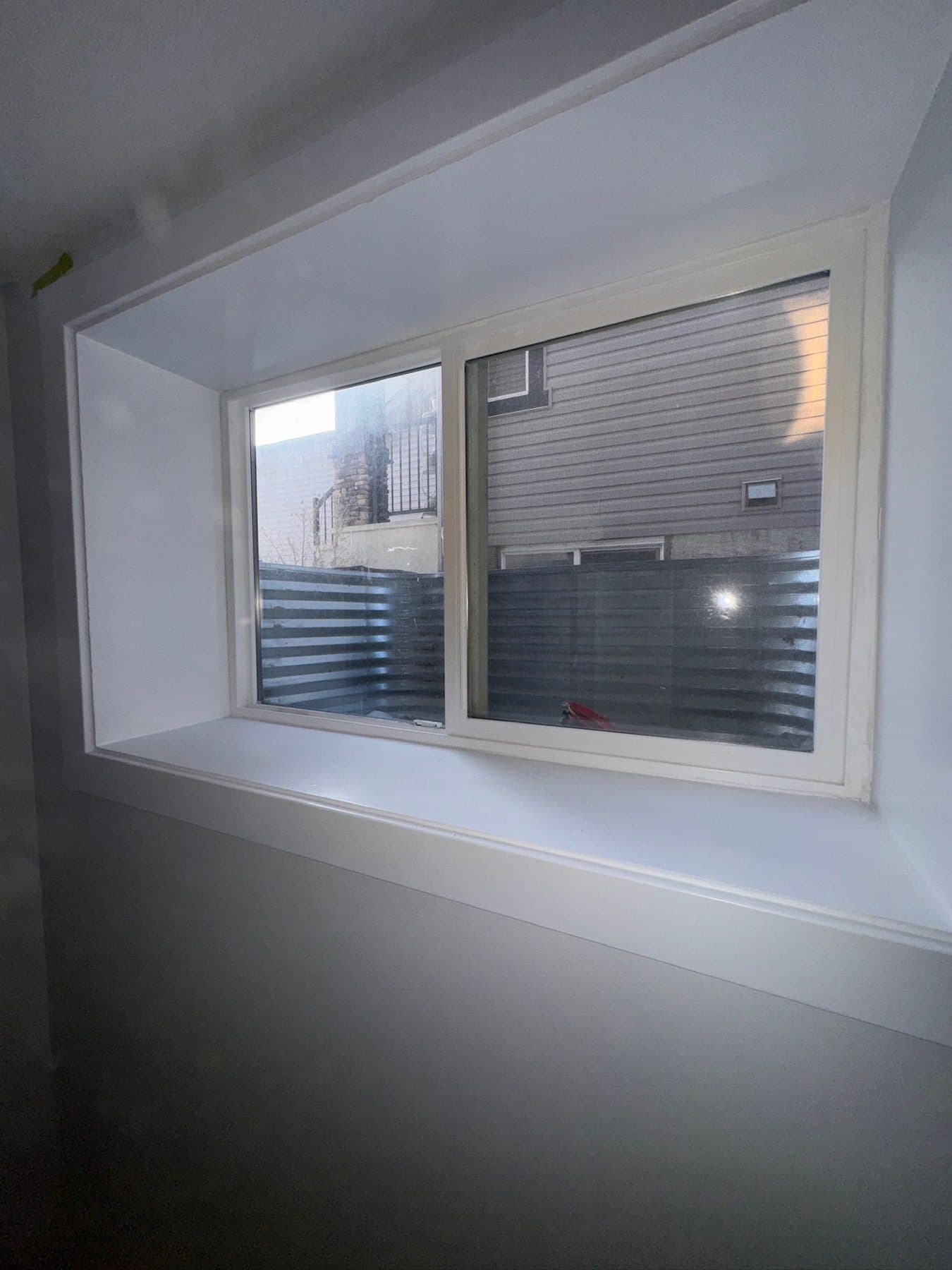 The same egress window after cleaning, with glass, frame, track and sill clear and daylight coming through.
