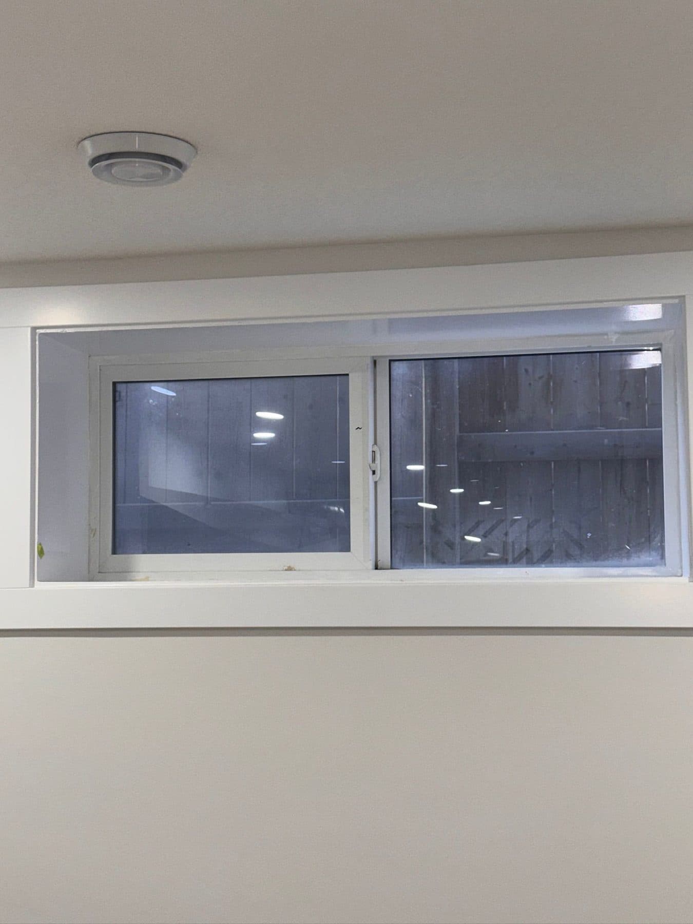 Basement egress window at site condition, glass and frame covered in construction dust and residue.