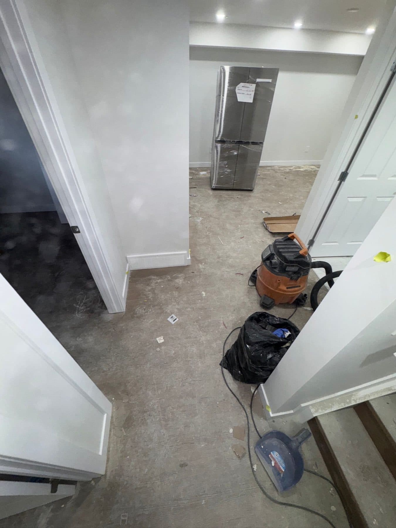 Utility area during construction with shop vacuums, tools and dust across a bare concrete floor.