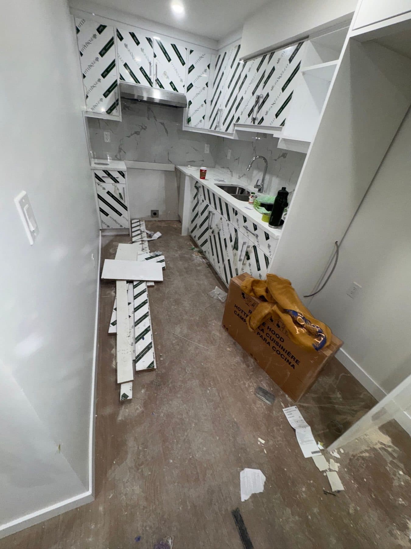 Suite kitchen at site condition: cabinetry still wrapped in protective film, packaging and offcuts on a bare floor.